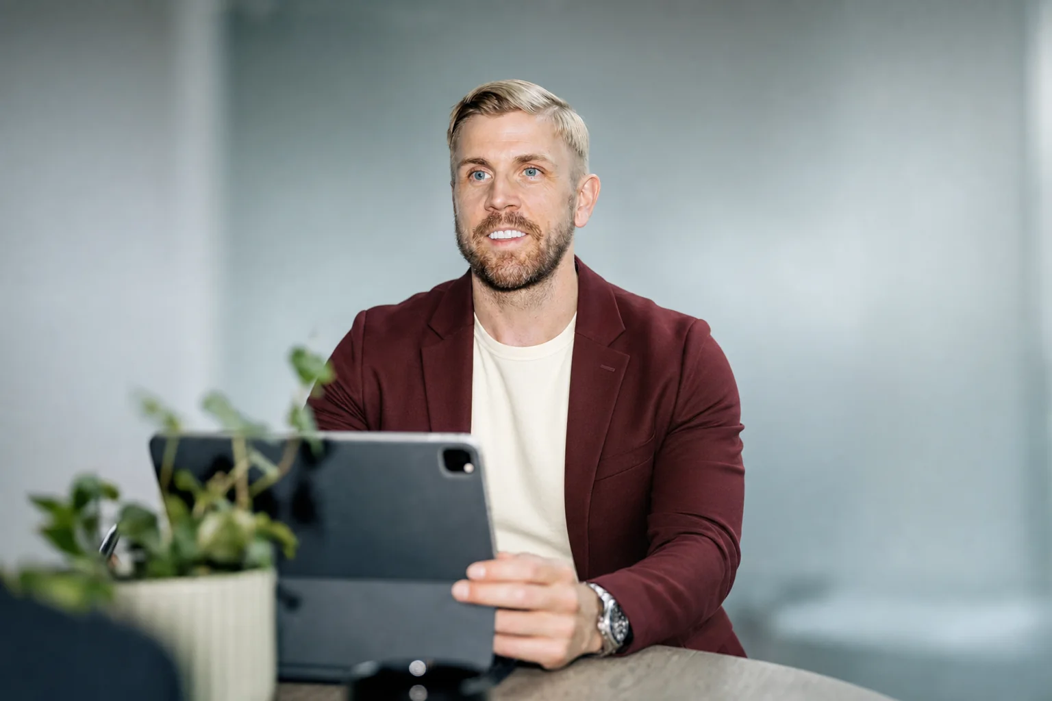 Nikk Matson in a burgundy blazer holding a tablet at a desk in an open-plan office